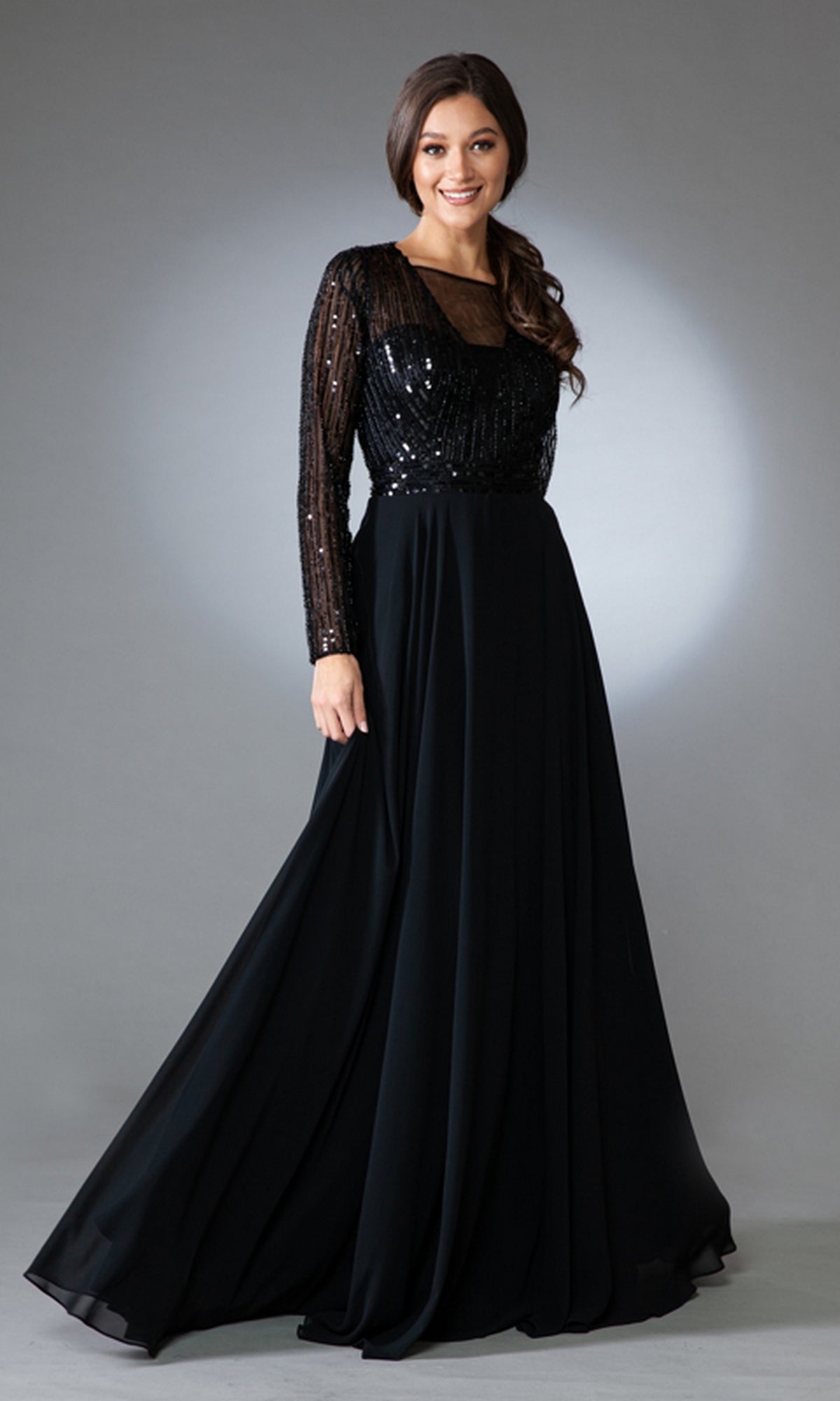 A woman models the Long-Sleeve Long Modest Prom Dress 7036, featuring sequin details on the fitted bodice and long sleeves, against a plain gray background.